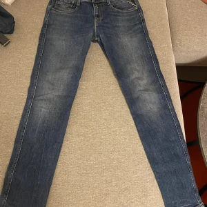 Replay Blå - Säljer ett par klassiska blå jeans från Replay med raka ben och snygga detaljer på bakfickorna. Jeansen har normal passform och är tillverkade i slitstarkt denimtyg. Perfekt för dig som gillar en enkel och stilren look.