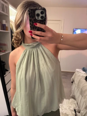 Glittrig ljusgrön halterneck topp från Zara - Säljer en superfin ljusgrön halterneck topp från Zara med glittrigt tyg. Toppen har en hög hals och är ärmlös, med ett flowy och luftigt fall. 