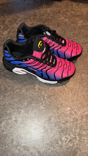 Nike Tn Barca - Nike Tns Patta edition med en fet gradient i rosa och blå, svarta detaljer och snörning. Snygga vågiga linjer på ovandelen och synlig Air Max-dämpning i sulan. Materialet är syntet med mesh och gummisula. Perfekt för dig som vill sticka ut med dina sneakers.