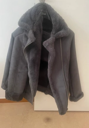 Mörkgrå teddyjacka från H&M Divided - Säljer en mörkgrå teddyjacka från H&M Divided i storlek S. Jackan har fluffigt foder, bred krage och muddar i samma mjuka material. Snygg asymmetrisk dragkedja framtill och två fickor. Perfekt för dig som gillar oversized och mysig stil.