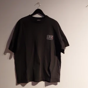 Svart Nas t-shirt från H&M oversized - Svart oversized t-shirt från H&M med Nas-logga på bröstet och stor färgglad grafisk print på ryggen med texten 'The world is yours 1994'. Skön passform och tillverkad i mjuk bomull. Perfekt för dig som gillar streetwear och hiphop-vibe. Ovanlig eftersom den inte går att hitta online i Sverige ny.