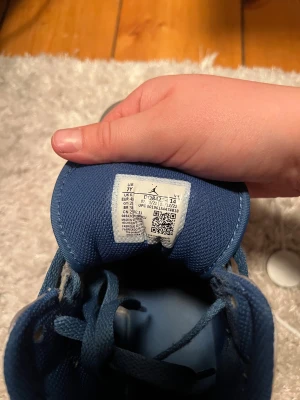 Nike Air Jordan 1 Mid grå/blå sneakers - Nike Air Jordan 1 Mid sneakers i grått och vitt skinn med blå detaljer och blå snörning. Klassisk Jordan-logga på sidan och tungan. Snygg kontrast mellan de olika färgblocken och den blå swooshen. Perfekta för dig som gillar streetstyle och ikoniska sneakers.