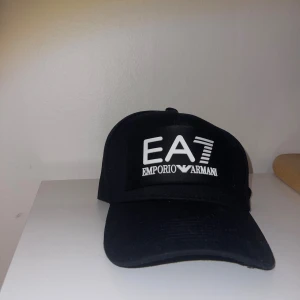 Snygg EA7 keps. - Säljer en svart EA7 keps som är i bra skick. Varan har ett stort tryck på framsidan.