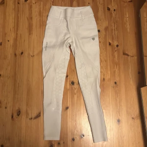 Vienna Compression Breeches Maya Delorez XS - Snygga vita ridbyxor från Maya Delorez i storlek XS. De har hög midja, praktiska fickor med knappar bak och silikongrepp längs insidan av benen för extra fäste. Materialet är stretchigt. Endast använd på tävling max 10 gånger så nyskick. De är i modellen  Vienna Compression Breeches