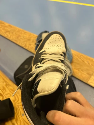 Nike Air Jordan 1 svart/vit mint - Nike Air Jordan 1 sneakers i svart och vit med mintgrön swoosh och Air Jordan-logga på sidan. Klassisk high-top siluett med snörning och perforerad tå. Skorna är tillverkade i skinn och har en platt sula. Perfekt för dig som gillar streetwear och vill sticka ut.