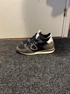 Philippe Model sneakers i mocka och tyg - Säljer ett par Philippe Model sneakers i mörkblått och grått med vita detaljer. Skorna har ovandel i mocka och skinn, klassisk snörning och rund tå. Snygg kontrast mellan material och färger, perfekt till jeans eller casual outfits även perfekt till kommande vår och sommar. Kommer med originalkartong och dustbag.