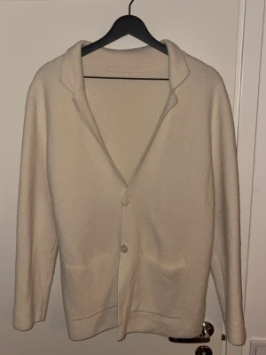 Beige kofta med fickor och knappar - En stilren beige kofta med två stora fickor framtill och klassisk krage. Storleken är S, passar längden 175-180