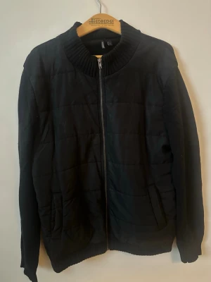 Svart quiltad bomberjacka med dragkedja - Säljer en svart bomberjacka från H&M med quiltad framsida och ribbad krage. Jackan har dragkedja framtill, två fickor och stickade ärmar och rygg. Perfekt för dig som gillar en enkel men ändå snygg look.