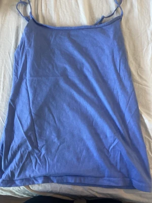 Blå linnetopp från Primark - Säljer en enkel blå linnetopp från Primark med tunna axelband. Toppen är stretchig och gjord i mjuk bomullsmix, perfekt för varma dagar. Passar dig som gillar en clean och avslappnad stil.