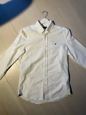 Vit skjorta från Morris - Nypris är 1300kr. Klassisk vit skjorta från Morris med lång ärm och diskret broderad logga på bröstet. Skjortan har knappar hela vägen och är tillverkad i mjuk bomull. Perfekt för en clean och stilren look.