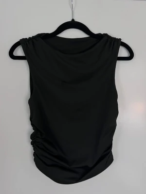 Svart ärmlös topp med rynkade sidor, storlek S - Svart svart ärmlös topp med snygga rynkade detaljer. Stilten med rund halsringning. Aldrig använd. - Köper du innan kl 16:00 kan jag posta samma dag!
