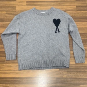 Grå stickad tröja från Ami - Säljer en stilren stickad tröja från AMI Paris i grå färg. Tröjan är mjuk, skön och mycket bekväm att bära – perfekt för vardagsbruk året runt. Tidlös design som passar lika bra till jeans som till mer uppklädda outfits. I fint skick.