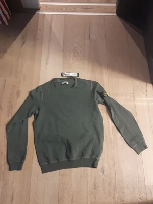 Grön sweatshirt från Stone Island L - Säljer en grön sweatshirt från Stone Island i storlek L. Tröjan har rund hals, ribbade muddar och den klassiska loggan på vänster ärm. Perfekt för dig som gillar stilrena och exklusiva plagg med streetkänsla. HELT OANVÄND LAPPEN ÄR KVAR O ALLT!