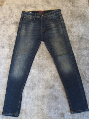 Jack & Jones Slim Tapered Erik jeans blå - Säljer ett par mörkblå jeans från Jack & Jones, modell Tapered/Erik. Jeansen har klassisk femficksdesign, snygga slitningar och kontrastsömmar. Passformen är tapered med smalare ben och normal midja. Perfekta till sneakers och hoodie eller skjorta för lite finare tillfällen👌