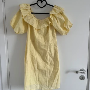 Gul kortklänning med volang från H&M - Supersöt ljusgul kortklänning från H&M i linnemix. Klänningen har puffiga korta ärmar, stor volang runt urringningen och en vacker passform. Perfekt för sommarens alla tillfällen.