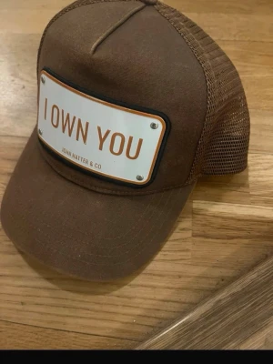 John hatter co. Keps - "I OWN YOU" är den perfekta kepsen och truckerkepsen för någon som inte är blyg för att göra ett djärvt uttalande om sig själv.