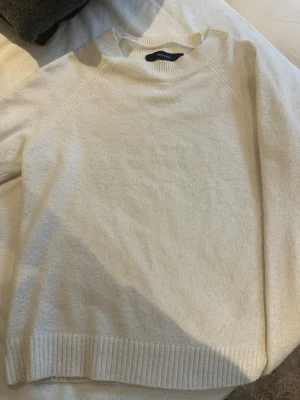 Vit stickad tröja från Vero Moda - Mysig vit stickad tröja från Vero Moda med ribbade muddar vid hals, ärmslut och nederkant. Enkel och stilren design som passar perfekt till lager på lager under kyliga dagar.