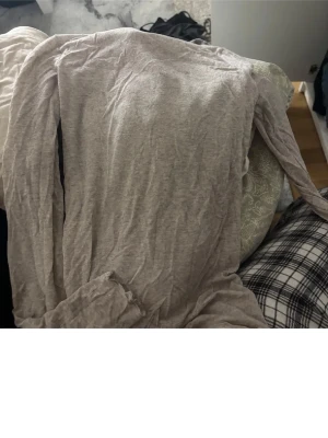 Beige omlottväst i bomull - Säljer en beige omlottväst i mjukt bomullsmaterial. Västen har långa band för knytning i midjan och en enkel, stilren design utan synliga knappar eller dragkedja. Perfekt att slänga över en t-shirt för en avslappnad look.