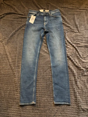 Tiger of Sweden blå jeans W30 L32 - Säljer ett par klassiska blå jeans från Tiger of Sweden i modellen W30 L32. Jeansen har fem fickor, raka ben och snygga slitningar framtill. Tillverkade i mjukt bomullsmaterial med en skön passform och läderpatch bak i midjan.