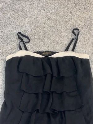Svart volang topp från Guess Jeans - Säljer en svart topp från Guess Jeans med tunna axelband och volanger framtill. Den är jättefin och i en lätt och luftig materiall. Den är i storlek S.