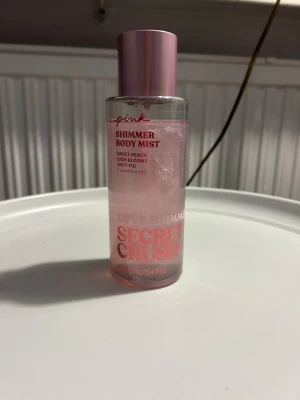Secret Crush Shimmer Body Mist - Shimmer Body Mist med doft av sweet peach, lush blooms och juicy fig. Innehåller eteriska oljor och ger en glittrande finish. Volym: 250 ml (8.4 fl oz). Perfekt för dig som vill ha extra glow i vardagen.