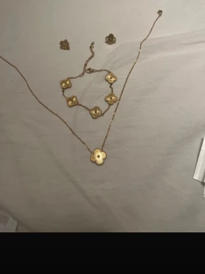 Fyrklöver 18k guldpläterade smycken set - Säljer ett snyggt smyckesset med halsband, armband, ring och örhängen i guld. Alla delar har fyrklöverformade hängen med guldkant. Haösband, armband och örhängen. Perfekt för dig som gillar stilrena accessoarer med en touch av lyx.