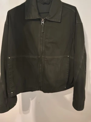 Denim jacka Zara - Säljer en mörkgrön denim jacka  med klassisk krage och raka linjer. Jackan har dragkedja framtill, två stora fickor med nitar och markerade sömmar som ger en clean look. Perfekt till en streetwear-outfit eller för att lyfta en enkel stil. Storlek Small