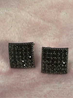 Glittriga fyrkantiga örhängen - Säljer ett par snygga fyrkantiga örhängen i mörkgrå med massor av små glittrande stenar på framsidan. De har en cool, lätt böjd form och push back-lås. Perfekta för dig som vill ha något som sticker ut lite extra.