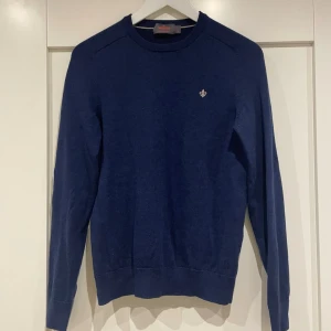 Marinblå stickad tröja från Morris - Säljer en marinblå stickad tröja från Morris med rund hals och diskret broderad logga på bröstet. Tröjan har långa ärmar och ribbade muddar vid ärmslut och nederkant. Perfekt för dig som gillar klassisk och stilren look.