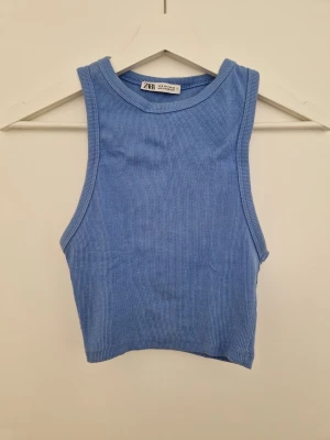 Blå ribbad linnetopp från Zara - Säljer en blå ribbad linnetopp från Zara i storlek S. Toppen är croppad och ärmlös med rund halsringning. Tillverkad i mjuk bomull med lite stretch för skön passform. Perfekt till jeans eller kjol för en enkel och snygg look.