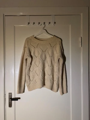Beige stickad tröja med strukturmönster - Säljer en beige stickad tröja med snyggt strukturmönster framtill och ribbade muddar. Tröjan har rund halsringning och långa ärmar. Perfekt för lager på lager under kyliga dagar.
