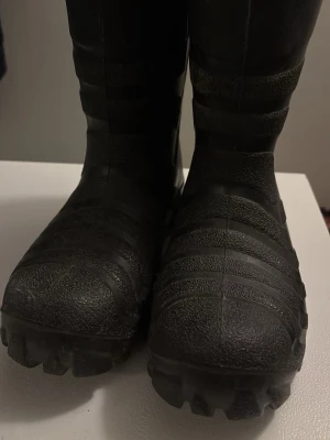 Viking svarta varma allvädersstövlar - Tunga svarta stövlar med grov sula och texturerad yta. Tillverkade i slitstark syntet, perfekta för blöta eller leriga dagar. Klassisk rund tå och högt skaft för extra skydd. Snygga och praktiska för höst och vinter.