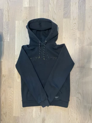 Svart hoodie - Peak Performance - Stilren Peak Performance hoodie i mörk färg med diskret logotyp framtill. Ett bekvämt och trendigt plagg som passar perfekt till en avslappnad vardagslook. Texten framtill är något utsuddad, vilket ger hoodien en vintage och worn-in känsla.  • Märke: Peak Performance • Typ: Hoodie • Färg: Svart • Passform: Regular fit • Skick: Bra begagnat skick • Text framtill, lite utsuddad (se bild) • Mjuk, tjock och bekväm kvalitet.                       Hör av dig vid intresse! Skickas snabbt!😊
