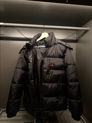 Svart pufferjacka från Polo Ralph Lauren - Säljer en svart pufferjacka från Polo Ralph Lauren med röd broderad logga på bröstet. Jackan har hög krage, dragkedja framtill och flera fickor. Tveka inte att höra av dig vid frågor och priset går att diskutera vid snabb affär😁