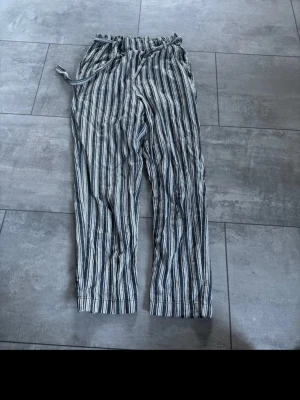 Randiga byxor med knytband - Säljer ett par luftiga byxor med svartvita ränder och elastisk midja med knytband. Perfekta för varma dagar och riktigt sköna att bära. Byxorna har raka ben och avslappnad passform.