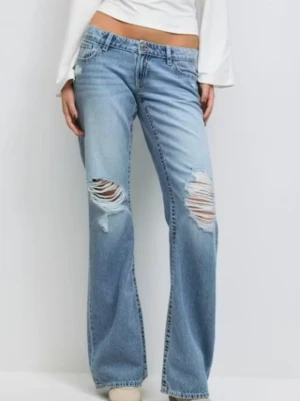 Ljusblå bootcut jeans med slitningar - Säljer ett par ljusblå bootcut jeans med snygga slitningar över knäna och lätt tvättad look. Jeansen har låg midja och klassisk femficksdesign. Tillverkade i mjukt jeansmaterial som ger en avslappnad vibe.