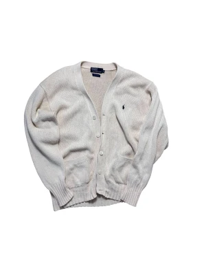 Vit kofta från Polo Ralph Lauren - Klassisk vit kofta från Polo Ralph Lauren i 100% bomull. Tröjan har v-ringning, knappar framtill, två fickor och den ikoniska broderade loggan på bröstet. Perfekt för lager på lager och enkel att matcha med allt.