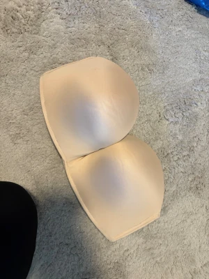 Beige bh utan band - Säljer en bh med slät yta och formade kupor. Toppen är axelbandslös och har en enkel, clean look som passar perfekt under kläder med bar rygg eller axlar. Materialet är mjukt och syntetiskt för en bekväm känsla.