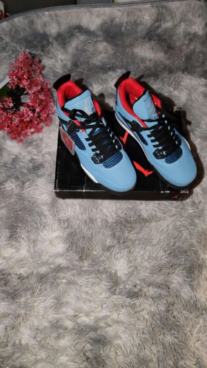 Nike Air Jordan 4 Travis Scott blå - Säljer ett par Nike Air Jordan 4 Travis Scott i blått med svarta och röda detaljer. Skorna har svart snörning, meshpaneler och en vit sula med synlig Air-enhet. Insidan är röd och hälen har Jumpman-logga. Perfekt för dig som vill sticka ut med en ikonisk sneaker.