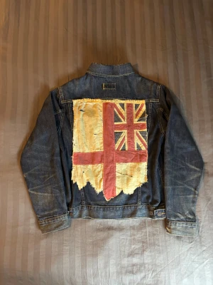 Ralph lauren denim&supply denim jeans jacka UK england - Tvär fet jeansjacka från ralph lauren denim&supply med UK/England flaggan där bak. Den ligger uppe på ebay för 160 euro vilket motsvarar 1750 sek. Fläckarna på flaggan är menade att vara där och är menade att ge jackan en vintage look. Sitter som S-M