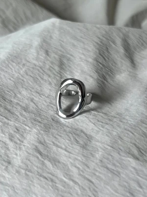 Assymetrical Oval - Justerbar ring i rostfritt stål med en ren, asymmetrisk ovalform. Minimal och modern.