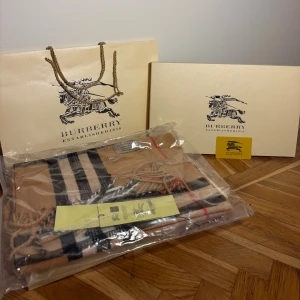 Burberry rutig kashmirhalsduk beige - Exklusiv halsduk från Burberry i klassiskt rutigt mönster med beige bas och inslag av svart, vitt och rött. Tillverkad i 100% kashmir för en supermjuk känsla. Perfekt accessoar med fransar i ändarna och ikonisk design. Levereras med originalförpackning och påse.