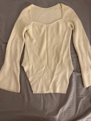 Beige ribbad långärmad topp - Säljer en beige ribbad topp med lång ärm och fyrkantig halsringning. Toppen har en figurnära passform och är tillverkad i ett stickat material som ger en mjuk och skön känsla. Perfekt att styla med jeans eller kjol för en clean look.