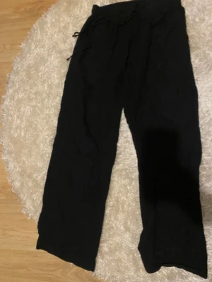 Svarta linnebyxor från Neo Noir, strl 36 - Svarta linnebyxor från Neo Noir i storlek 36. Byxorna har en loose passform, breda ben och snörning i midjan. Lite slitningar ner till. Ny pris 600kr