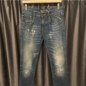Replay blå slitna jeans herr - Snygga blå jeans från Replay med slitna detaljer och lätt tvättad look. Klassisk femficksmodell med Replay-logga på fickan och läderpatch bak. Jeansen har raka ben och normal passform, tillverkade i tålig bomullsdenim.