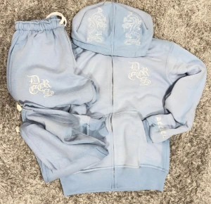 Decrese Sweden Set i Ljusblått  - Unisex hoodie + byxor i mjuk bomull med lätt stretch och stentvättad finish. Vit broderad logga och detaljer. Byxor: midja 30–42 cm, innerben 68 cm, ytterben 94 cm, 2 fram- och 2 bakfickor, resår+dragsko. Hoodie: axel 50 cm, bröst 50 cm, längd 64 cm, ärm 60 cm, 2 fickor. 🔥Intresserad? Det finns olika 📏🔥storlekar, så säg vilken du vill ha.” Skickas inom 1–2 dagar. Köparen står för returfrakt. 