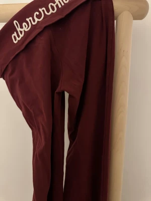 Vinröda leggings från Abercrombie - Vinröda leggings från Abercrombie med broderad logga i vitt på linningen och en liten älgdetalj. Byxorna har rak passform och är tillverkade i mjukt bomullsmaterial. Abercrombie kids storlek XL passar som vuxen S.