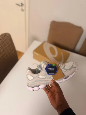 Asiks sneakers i ljusgrått - Säljer ett par sneakers i ljusgrått och vitt med mesh och mockadetaljer. Skorna har chunky sula med vita och grå inslag, samt snörning för perfekt passform. Perfekta för dig som gillar sportig och trendig stil.