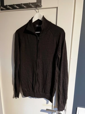 Mörkbrun kofta i merinoull  - Snygg mörkbrun kofta från Dressmann i mjuk merinoull. Modellen har hel dragkedja framtill, ribbad krage och muddar vid ärmslut och nederkant. Perfekt för lager-på-lager och chill stil. Passar dig som gillar klassiska och enkla plagg. Storlek M men skulle säga mitt emellan M-S. Använd 1 gång och tvättad efter de o sen aldrig använd.