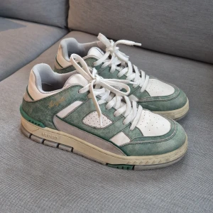 Axel Arigato gröna och vita sneakers - Snygga sneakers från Axel Arigato i storlek 42. Nypris 3500. Skorna har en fräsch kombination av grönt och vitt med detaljer i mocka och skinn. Klassisk rund tå, platt sula och snörning framtill. Perfekt för dig som gillar stilrena och trendiga sneakers med cool retrovibe.
